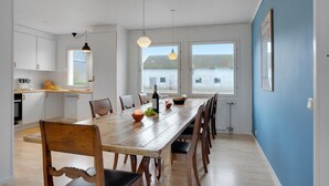 Une salle à manger spacieuse, avec une longue table en bois, de nombreuses chaises et une vue sur un paysage rural grâce à de grandes fenêtres.