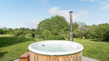 Un bain à remous en bois, avec un poteau en métal, entouré d’une zone herbeuse et d’arbres.