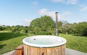 Ein hölzernes Whirlpool mit Metallstange, umgeben von einer Rasenfläche und Bäumen.