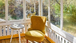 A yellow chair and a small table with glasses on a wooden deck, overlooking a garden with trees and a fence. - 2 bedroom amazing home in Kolmården (Kolmården)