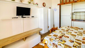 Ein Schlafzimmer mit Fernseher, einem Bett mit Kaffeemotiv, einer Holzbank, einem Kleiderschrank und einer Küchenzeile mit Herd.