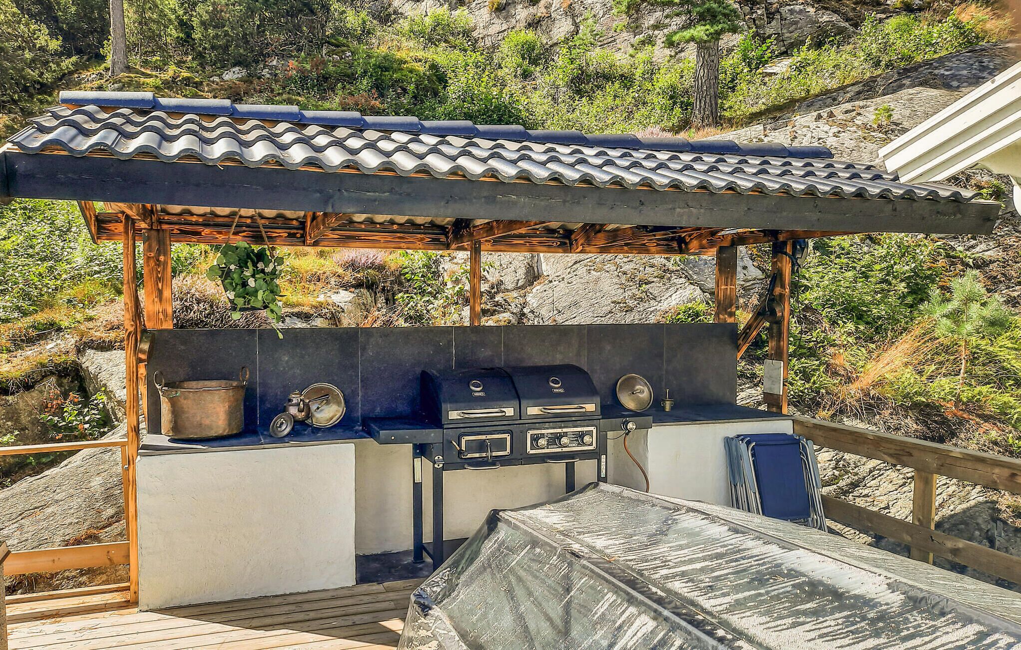 Un área de barbacoa al aire libre con techo de baldosas, una parrilla y un lavamanos.