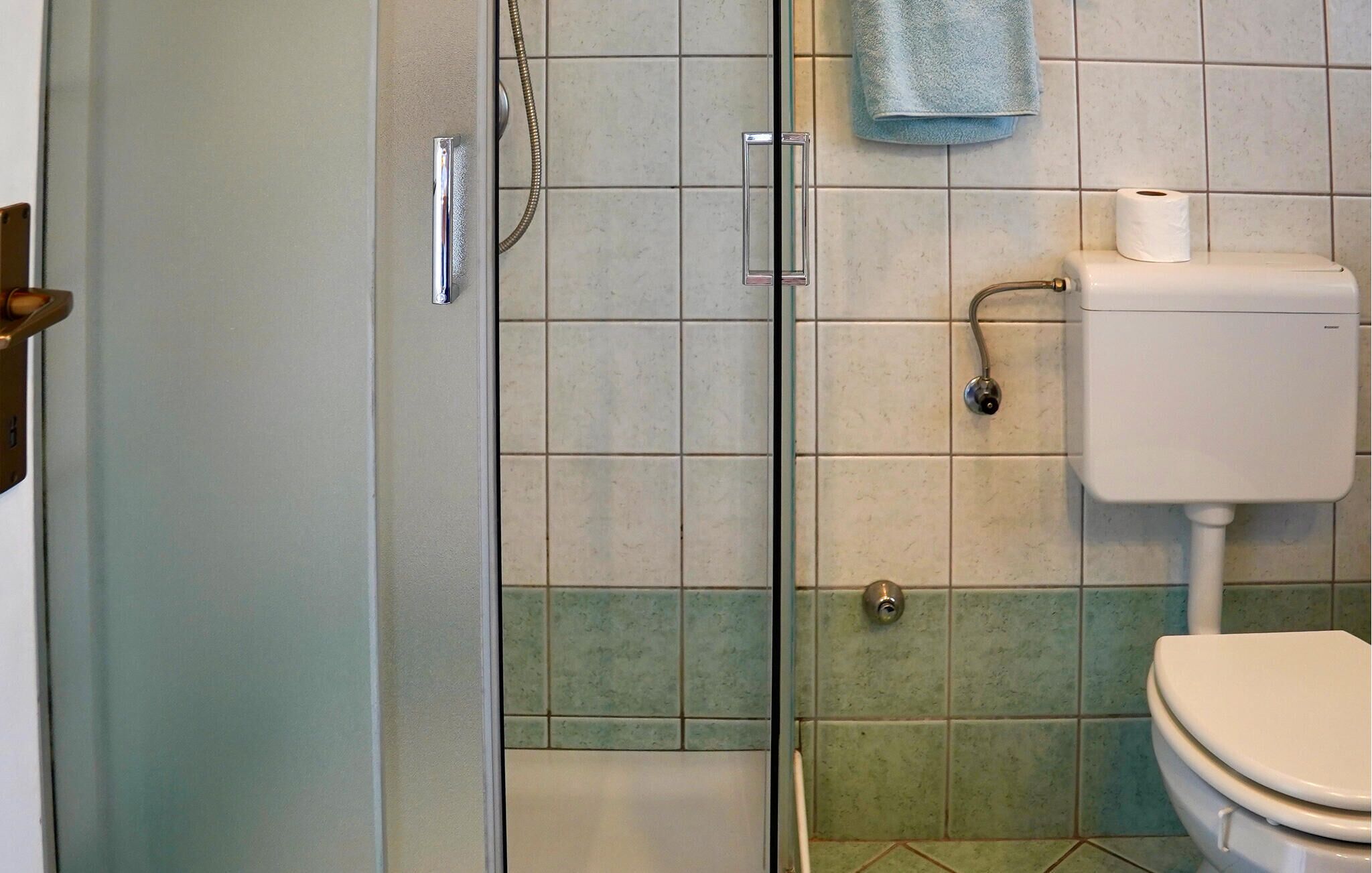 A bathroom with a glass shower door, a toilet, and a towel hanging on the wall.