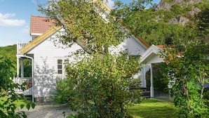 A white house with a red-tiled roof, surrounded by lush greenery and a wooden deck. - 4 bedroom beautiful home in Farsund (Farsund)