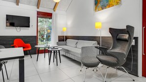 Een moderne woonkamer met een grijze bank, een rode fauteuil, een ronde tafel en een aan de muur bevestigde televisie.