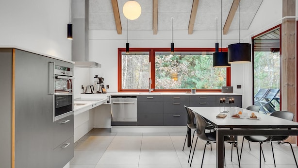 Een moderne keuken met een eethoek, grote ramen en uitzicht op bomen.