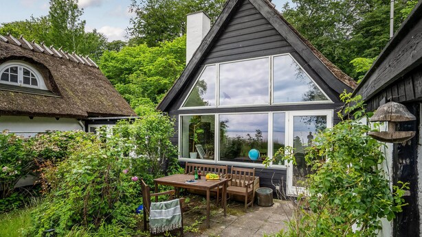 Une maison avec un toit de chaume et une extension moderne dotée de grandes fenêtres.