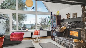 Un salon chaleureux avec une cheminée en pierre, une grande fenêtre donnant sur un paysage magnifique et un coin salon confortable.