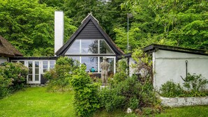 Une maison avec une grande fenêtre en verre, une cheminée et un jardin.