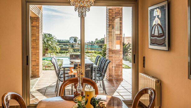 A dining area with a table set for four, a chandelier, and a view of a pool and garden.