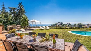 An outdoor dining area with a view of the ocean, a pool, and a gazebo.