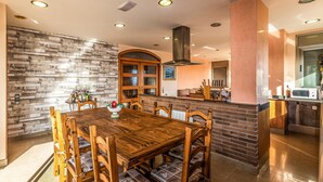A modern kitchen with a wooden dining table and chairs, a brick accent wall, and recessed ceiling lights.