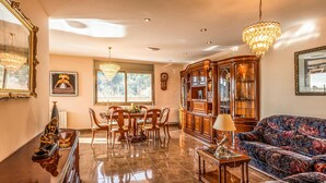 A spacious living room with a dining area, a chandelier, and a large cabinet.