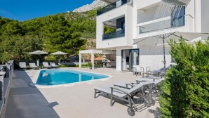 Une maison moderne à deux étages, dotée d’une piscine, d’un espace extérieur aménagé et offrant une vue sur les montagnes.