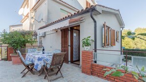 Ein zweistöckiges Haus mit einer Terrasse, auf der ein Esstisch, ein Stuhl und ein Blumentopf stehen.
