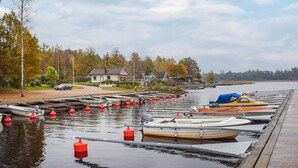 A marina with several boats docked, a dock extending into calm water, and houses in the background.