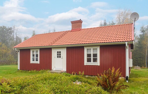 A red wooden house with a tiled roof, white windows, and a satellite dish.