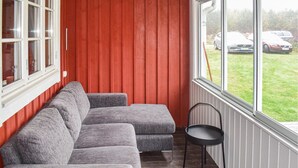 A room with a grey sectional sofa, a small black chair, and a window with a view of parked cars and greenery outside. - Cozy home in Ryd with WiFi (Ryd)