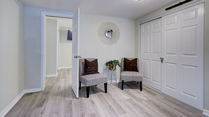 Un couloir avec deux fauteuils rembourrés, un miroir décoratif et une armoire blanche.