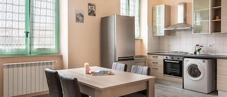 A modern kitchen with a dining area, featuring a refrigerator, oven, washing machine, and a window with a view.