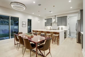A modern kitchen with a central island, pendant lighting, and a dining area with a glass table and chairs.