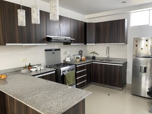 A modern kitchen with dark wood cabinets, a granite countertop, stainless steel appliances, and pendant lighting. - The palace  (Lambayeque)