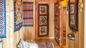 Interior acolhedor de uma cabana de madeira, com uma cama, tapetes coloridos e uma porta de madeira com painéis decorativos.