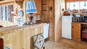 Interior de uma cabana de madeira com cozinha, incluindo frigorífico, micro-ondas e diversos utensílios de cozinha.