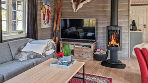 A cozy living room with a sofa, a coffee table, a flat-screen TV, a fireplace, and wooden walls. - Stunning home in Hovden i setesdal (Hovden i setesdal)