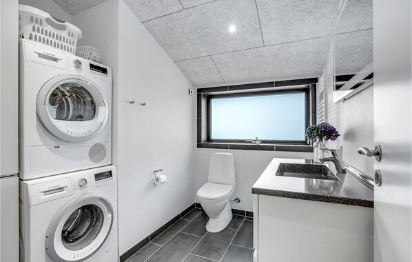 A compact, modern bathroom with a Bosch washing machine, a toilet, and a sink with a window above. - Stunning home in Blåvand with WiFi (Blåvand)