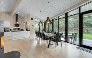 A modern kitchen with a central island, a dining area with a large table and chairs, and large windows offering a view of the outdoors. - Stunning home in Blåvand with WiFi (Blåvand)