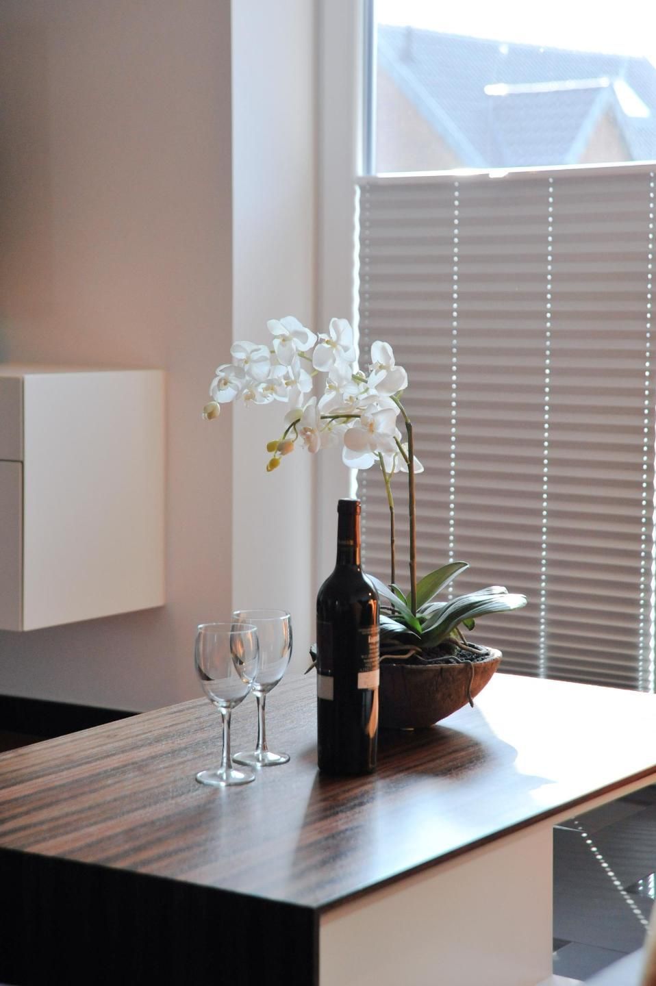 A wooden table with a bottle of wine, two glasses, and a potted orchid.