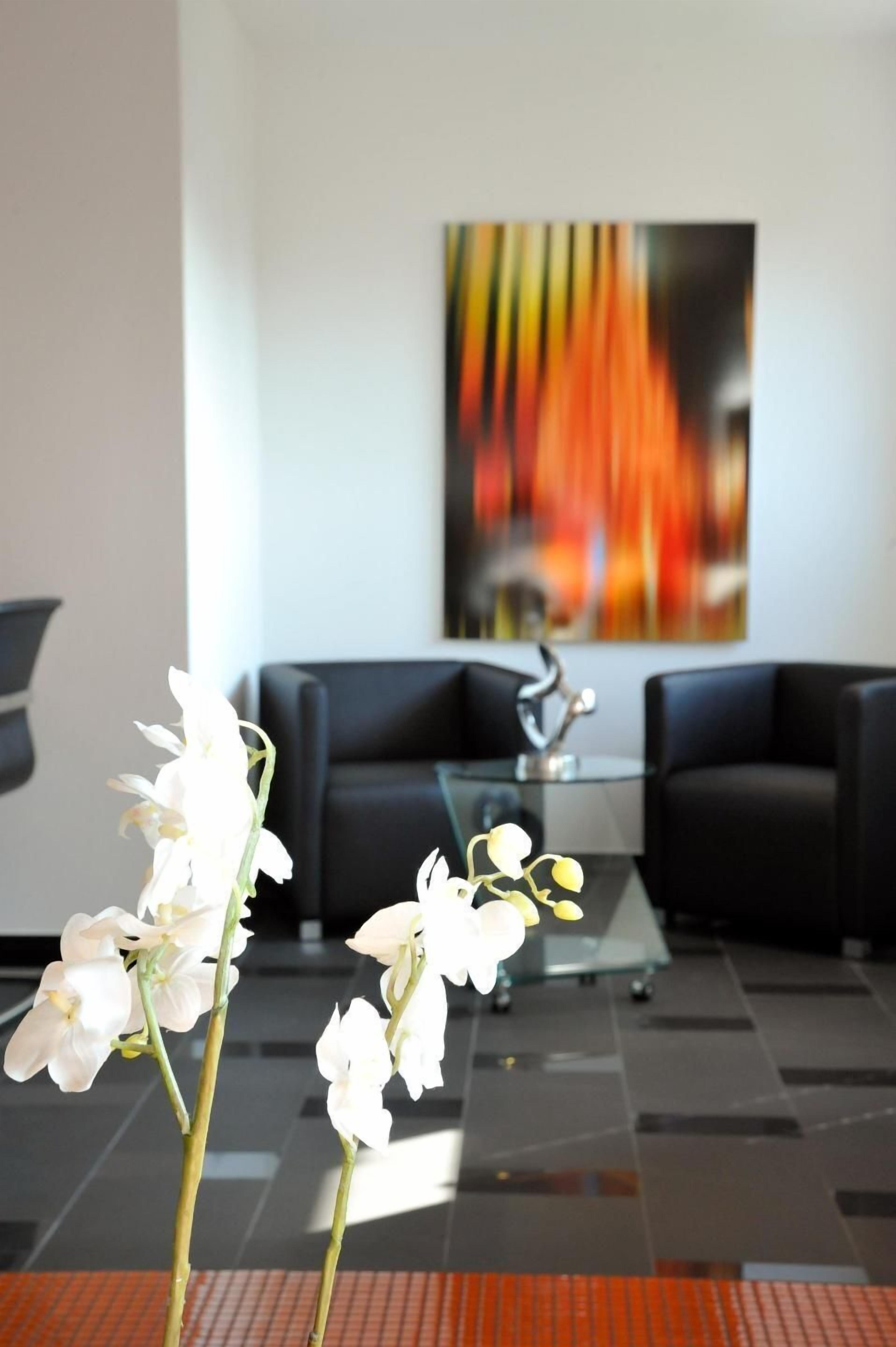 Een modern interieur met een glazen salontafel, zwarte banken en een levendig abstract schilderij aan de muur.