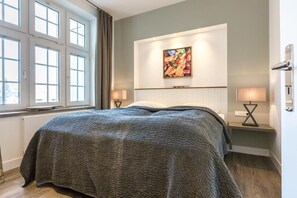 A bedroom with a large bed, two bedside tables with lamps, a window with curtains, and a painting on the wall.