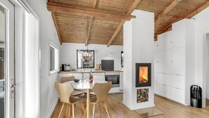 Una cocina moderna con una estufa de leña, un comedor con mesa y sillas, y una pared de ladrillo blanco.