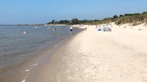 Una playa con gente nadando y caminando por la orilla, algunas sombrillas y una costa distante con edificios.
