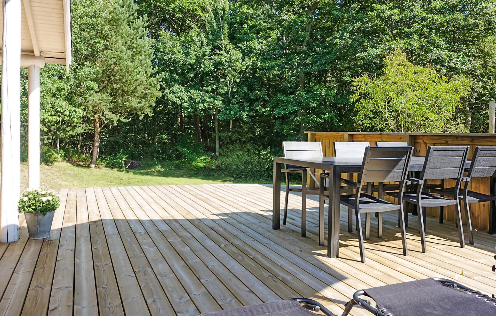 Une terrasse en bois avec une table et des chaises, entourée d’une végétation luxuriante.