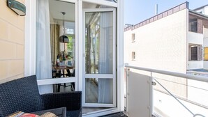 En balkong med ett matbord och stolar, en soffa i rotting och en skjutdörr i glas som leder in till ett inomhusutrymme.