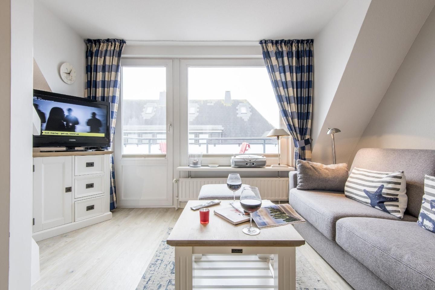 A cozy living room with a television, a sofa, a coffee table with drinks, and a view of the city through large windows.