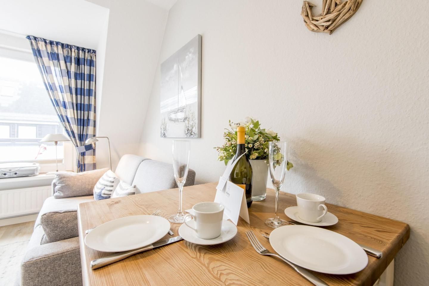 A dining table set with plates, cutlery, a vase with flowers, and a bottle of champagne.