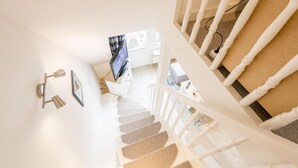 Un escalier avec des balustrades blanches, un téléviseur à écran plat fixé au mur et un luminaire mural.