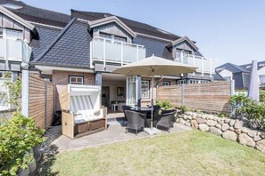 A residential house with a patio area featuring outdoor furniture and a covered seating area. - Hell. Zentral. Garten. - Haus Nordmarkgarten, Whg. 2 - Objekt-id: Hng/02 - Haus Nordmarkgarten (Sylt)