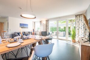 A modern dining area with a wooden table, chairs, and a view of a garden through large windows.