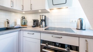 Una cocina moderna con armarios blancos, una cafetera de acero inoxidable, un hervidor y un horno empotrado.