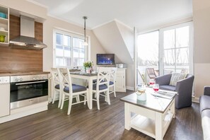 A modern kitchen with a built-in oven and a dining area with white chairs. - House Nordhedig 1, Whg. 4 - House Nordhedig (Sylt)