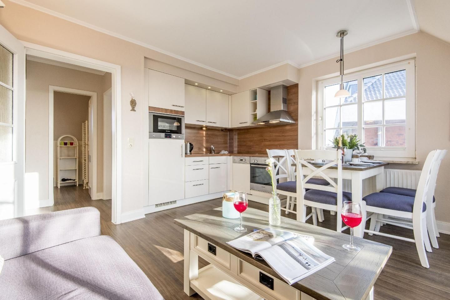 A modern kitchen with white cabinets, a microwave, and a stove. There is a dining area with a table and chairs, and a window with a view of the outside.