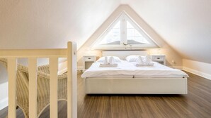 Ein Schlafzimmer mit schrägverdachter Decke, einem Bett mit weißen Leinentüchern, zwei Nachttischen und einem Fenster mit Blick.
