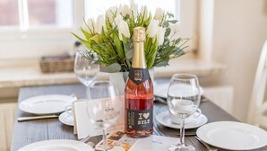 Ein gedeckter Tisch mit einem Essen, einer Flasche Rotwein, weißen Tellern und einem Strauß weißer Blumen.
