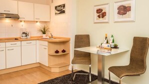 Una cucina moderna con mobili bianchi, una macchina da caffè e un'area pranzo con due sedie in vimini e un tavolo.