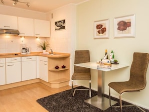 Una cocina moderna con armarios blancos, una cafetera y un comedor con dos sillas de mimbre y una mesa.